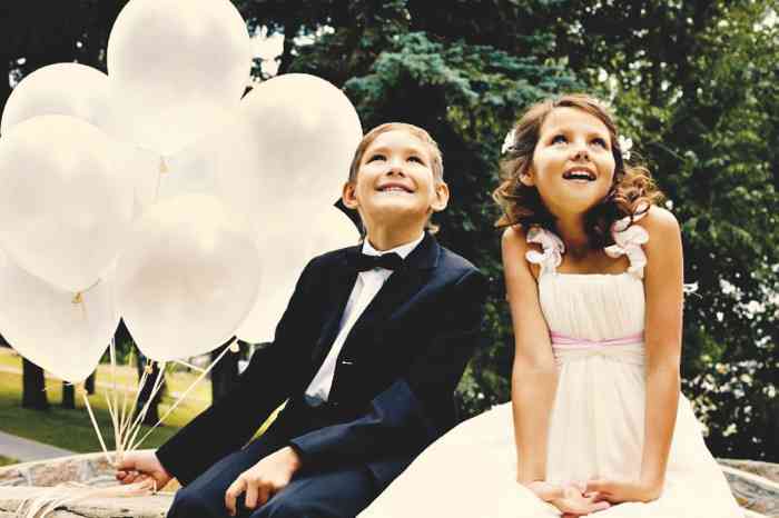 Weiße Luftballons, ein Mädchen und ein Junge in festlichem Hochzeits-Outfit.