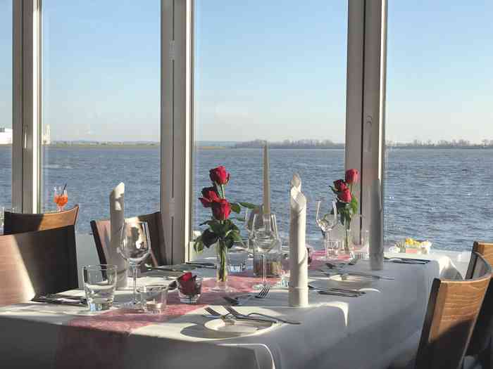 Hochzeitslocation Restaurant Fischclub Blankenese. Festlich gedeckter Tisch mit roten Roden. Aus dem Fester sieht man das Elbpanorama.