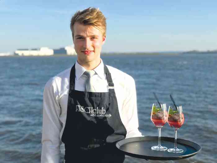 Ein Kellner serviert Getränke. Im Hintergrund die Elbe beim Restaurant FISCHclub Blankenese.