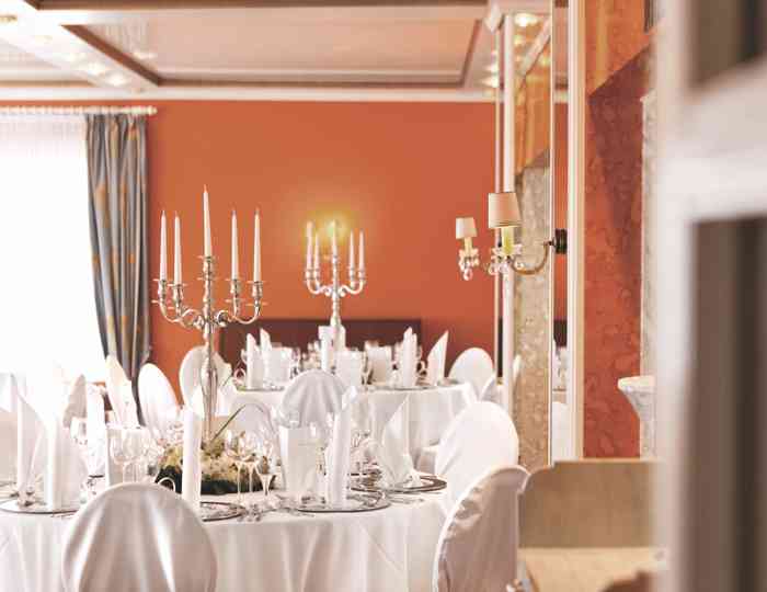 Hochzeitslocation Strauers Hotel am See am Plöner See. Saal mit weiß eingedeckten Tischen und Kerzenleuchtern