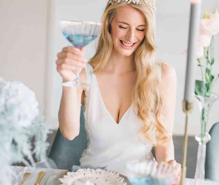 Braut erhebt Glas mit blauem Getränk.