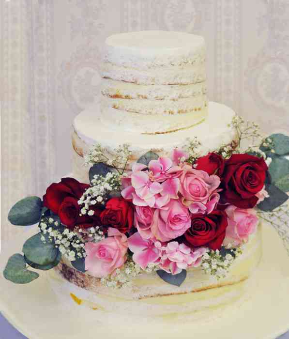 Diese Naked-Cake Hochzeitstorte sieht doch einfach umwerfend aus! Jedes Stockwerk kann eine andere Geschmacksvariante beinhalten. Die üppige Rosendekoration verleiht dem leicht-luftigen Schmuckstück die edle Eleganz.