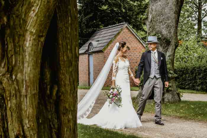 Das Brautpaar spaziert händchenhaltend durch einen Park.