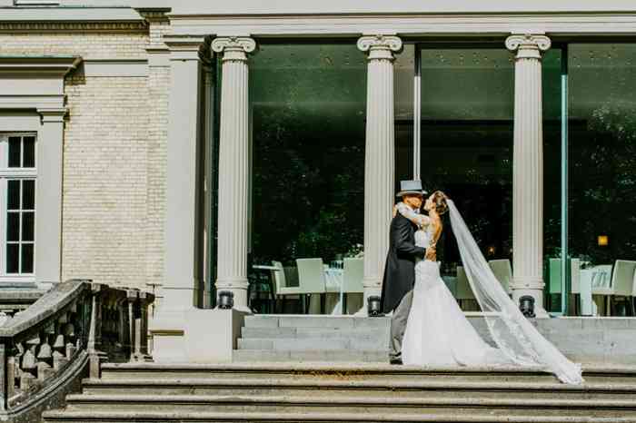 Brautpaar steht küssend vor der großen Fensterfront der Hochzeitslocation Elblounge.