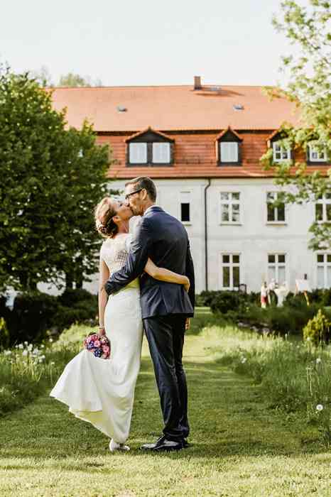 Das Hochzeitspaar steht küssend im Garten vor Schloss Neuenhausen.