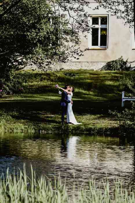 Hochzeitspaar steht vor einem Teich im Garten von Schloss Neuenhausen.