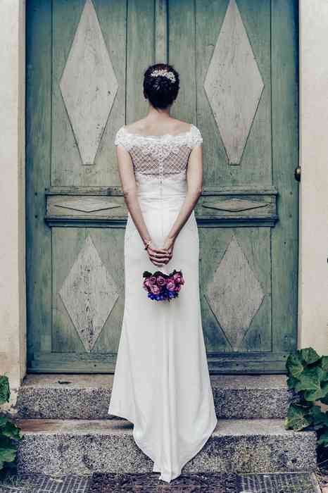 Die Braut in ihrem Hochzeitskleid von hinten vor einer schön bemalten Holztür.